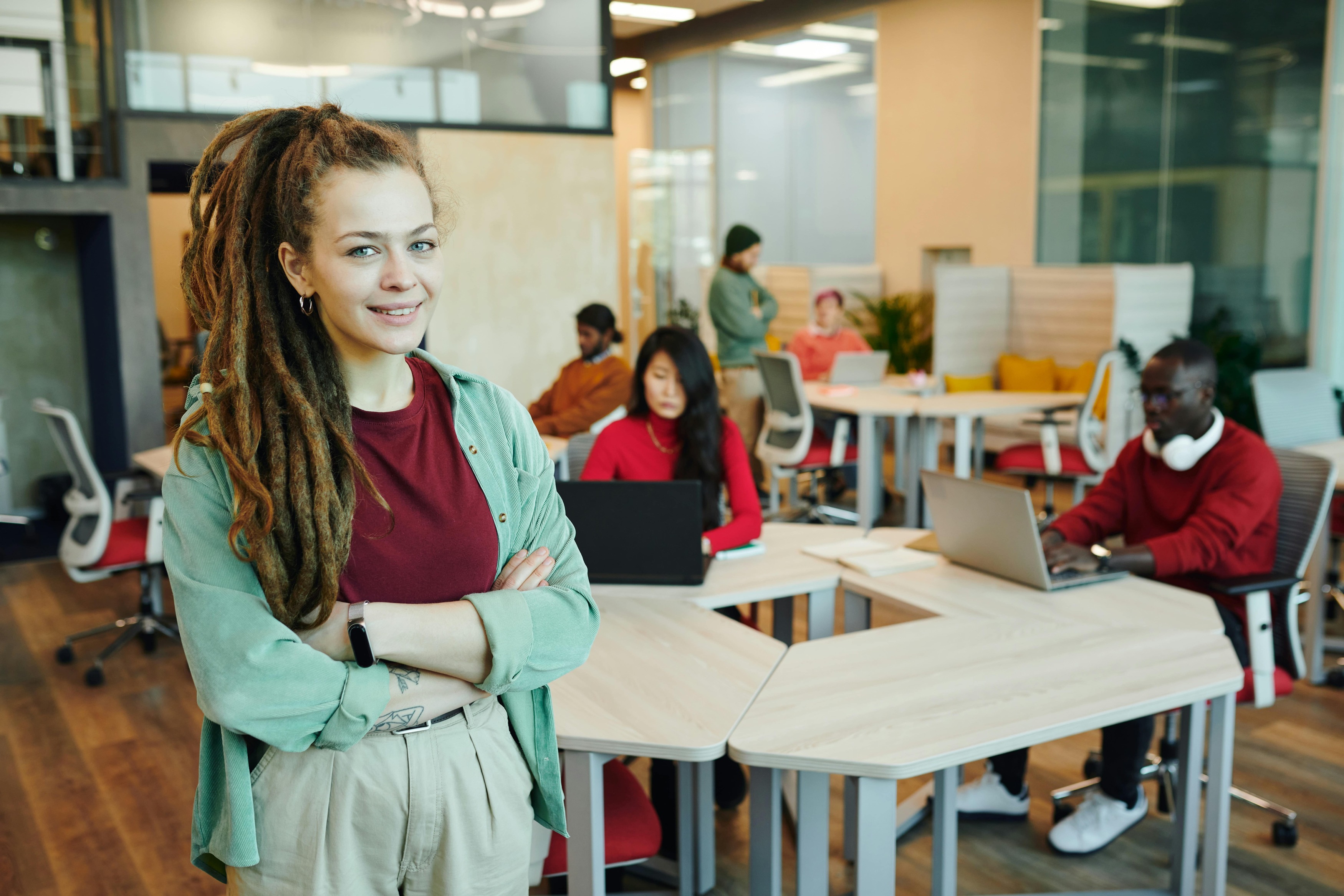 Jeune femme souriante avec des dreadlocks dans un espace de travail collaboratif moderne, entourée d'une équipe diverse travaillant sur des ordinateurs portables